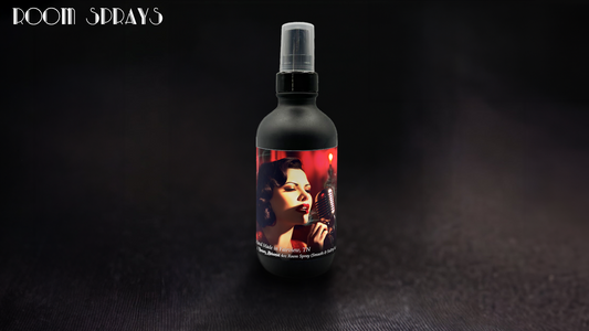 Black room spray bottle with spray cap featuring a vintage-style woman singing into a microphone on the label, displayed on a dark wood surface.

